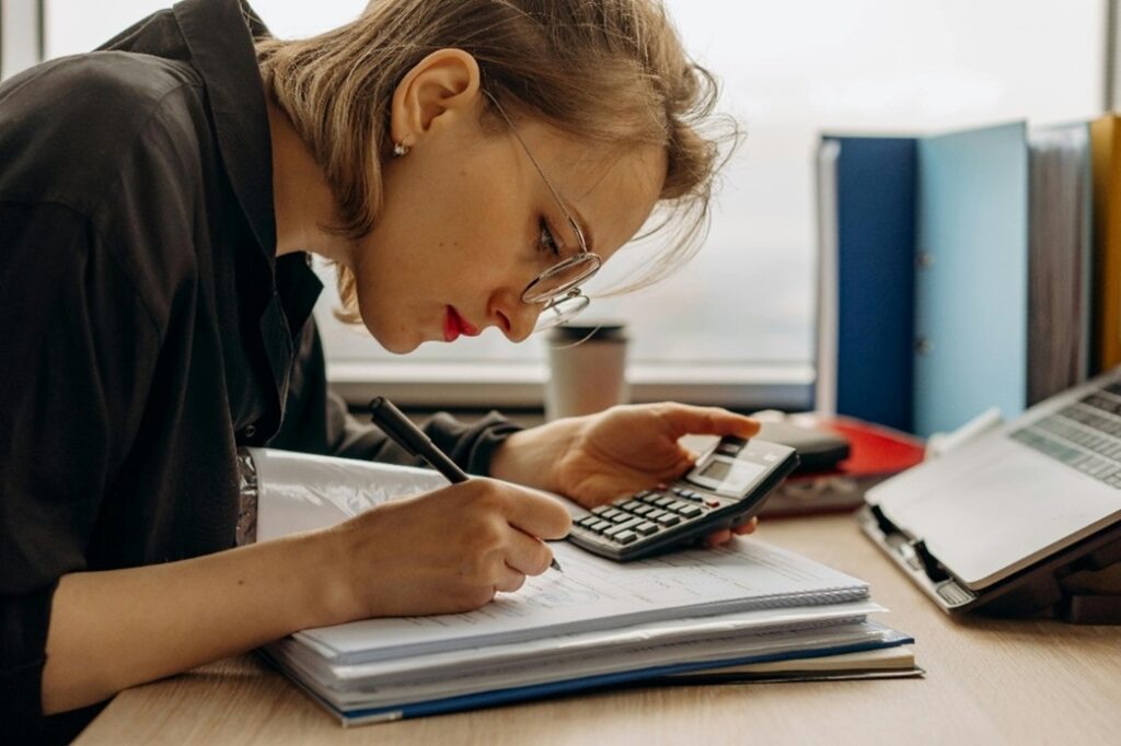 Woman peering over calculator with a file of papers